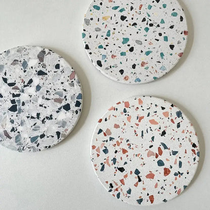 Three circular decorbites diatomite coasters with terrazzo pattern in white black gray teal and muted pink tones for dining use