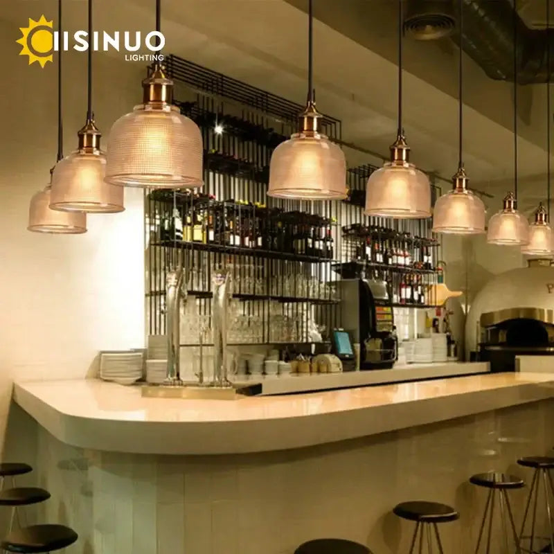 Warm-toned textured amber gold and teal glass pendant lights with brass accents hang above a modern bar area