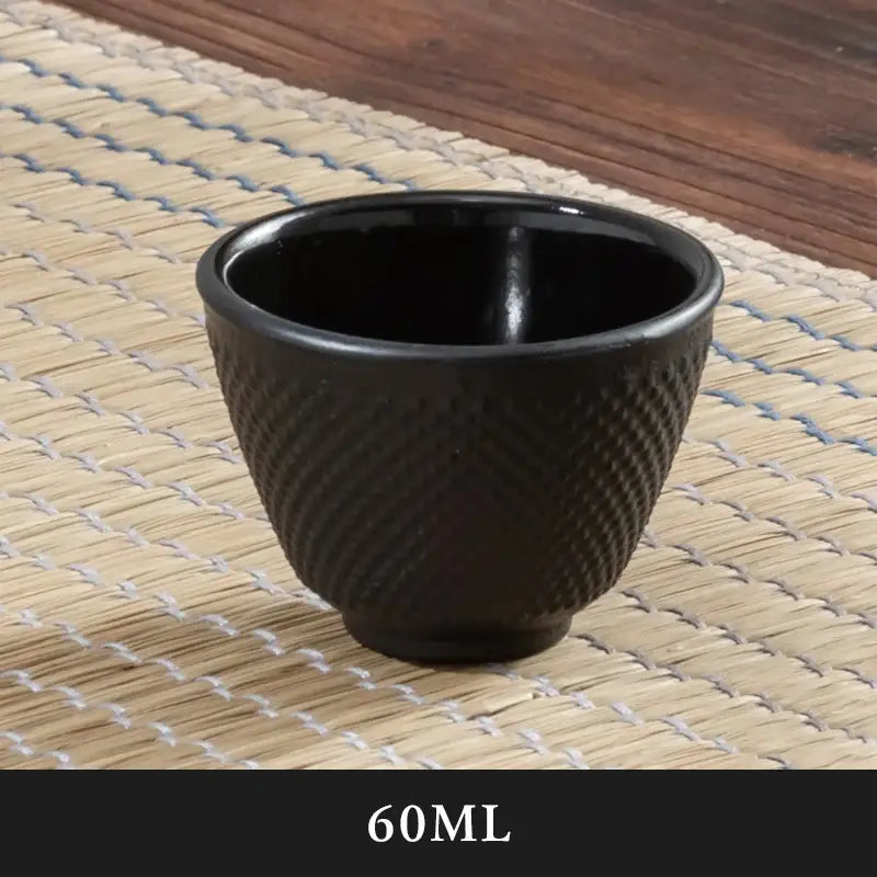Black ceramic teacup with textured diamond pattern and glossy finish paired with cast iron tea pot and infuser steeper