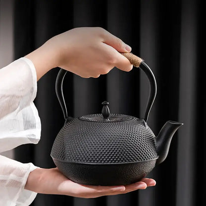 Textured black cast iron tea pot with dimpled surface and cork wrapped handle featuring built in infuser steeper