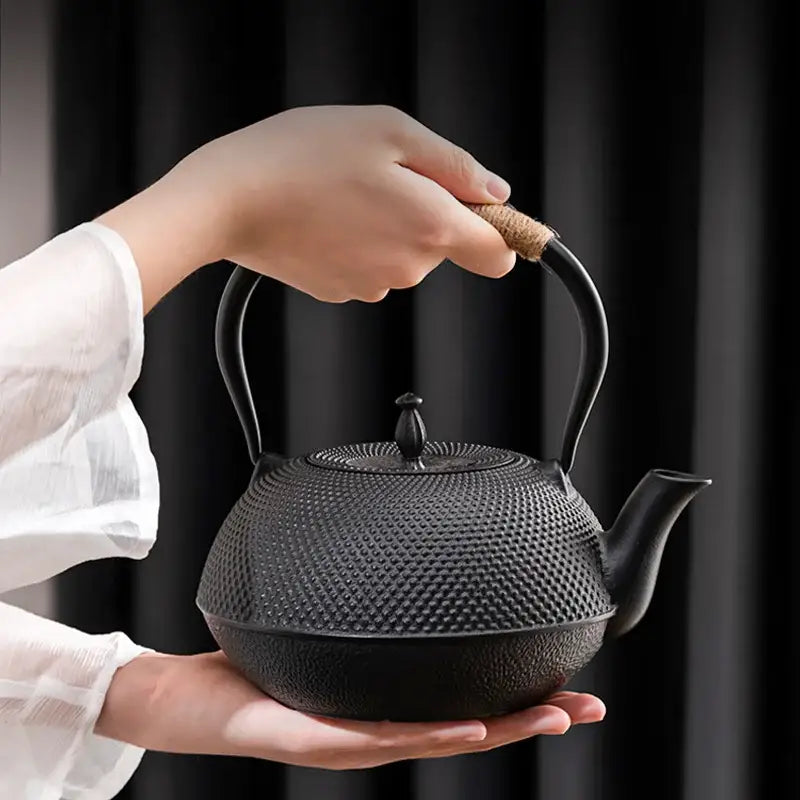 Textured black cast iron tea pot with dimpled surface and cork wrapped handle featuring built in infuser steeper