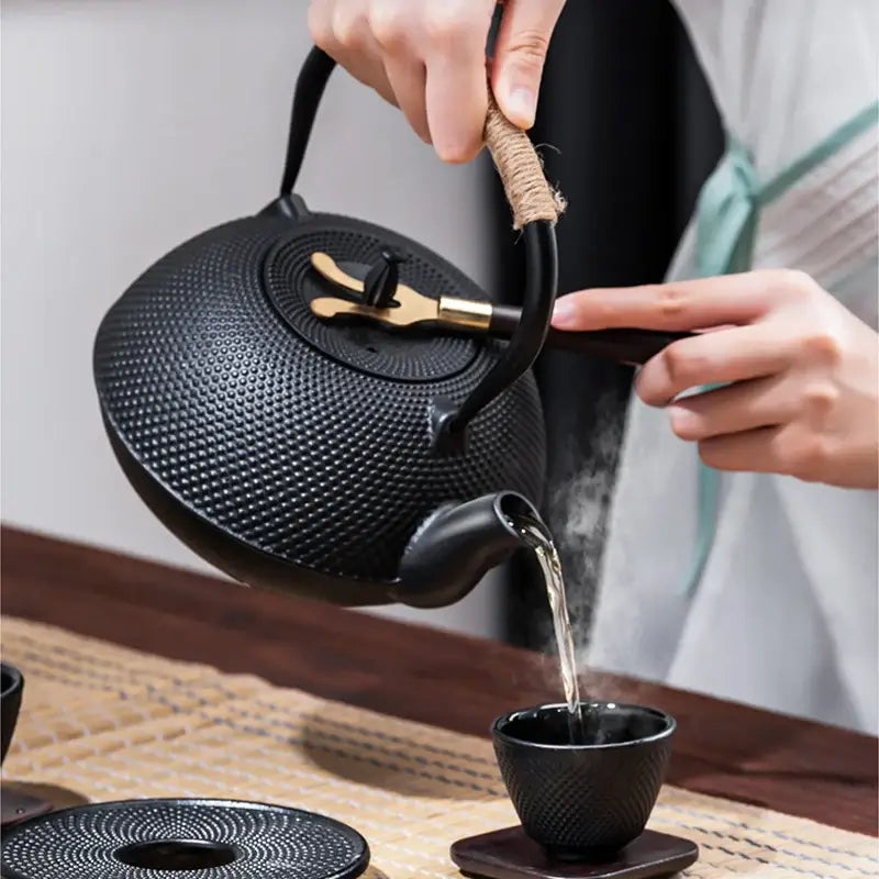 Textured black cast iron tea pot with brass accents on lid and handle designed for kitchen steeping use with infuser