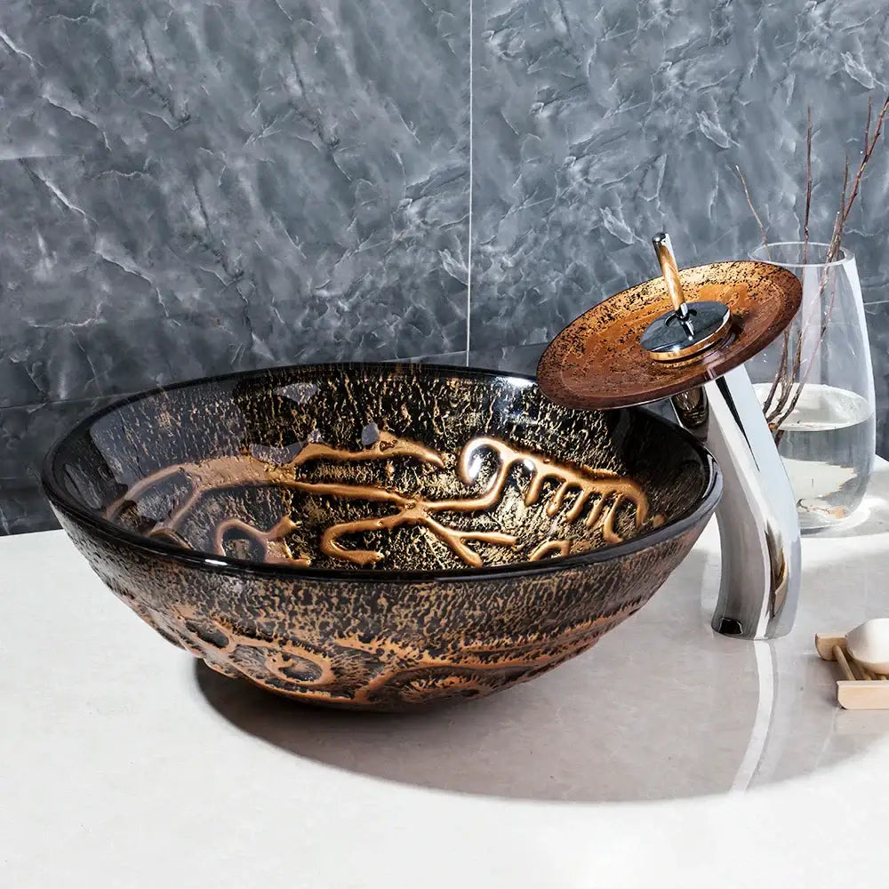 Glossy black glass wash basin set with intricate gold leaf patterns and matching bronze waterfall faucet for bathroom