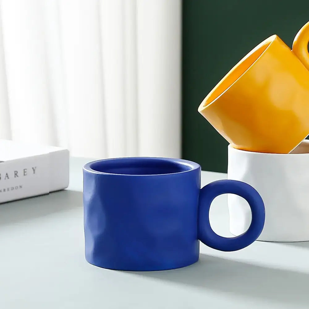 A vibrant blue ceramic coffee mug with a textured hammered finish and a circular handle for daily use