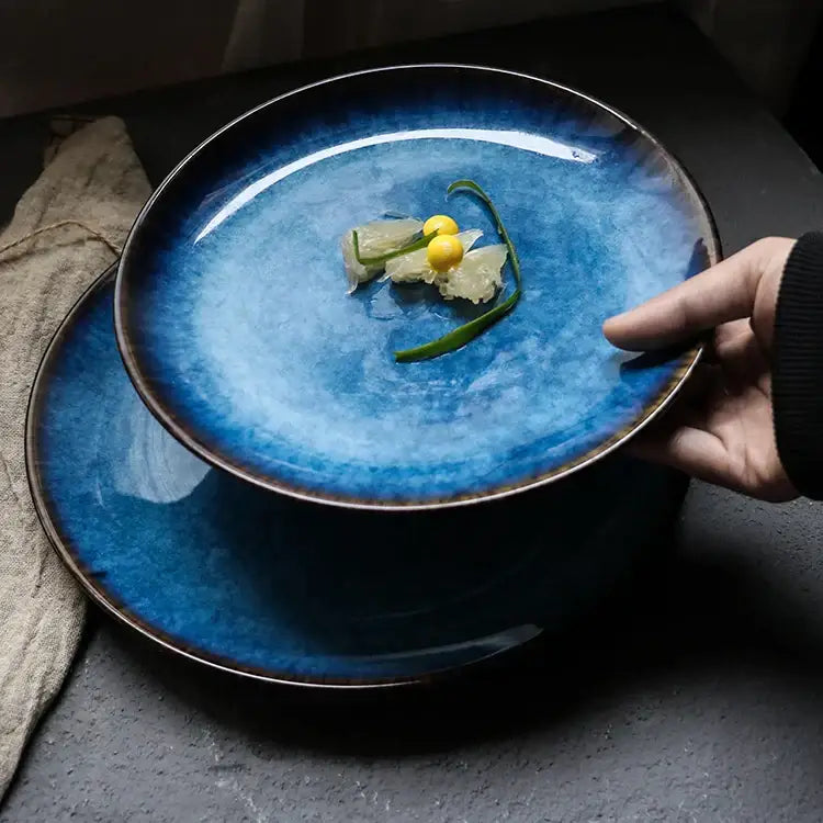 A hand holds a deep blue textured ceramic dinner plate with gradient glaze and dark brown rim from decorbites dinner plate set