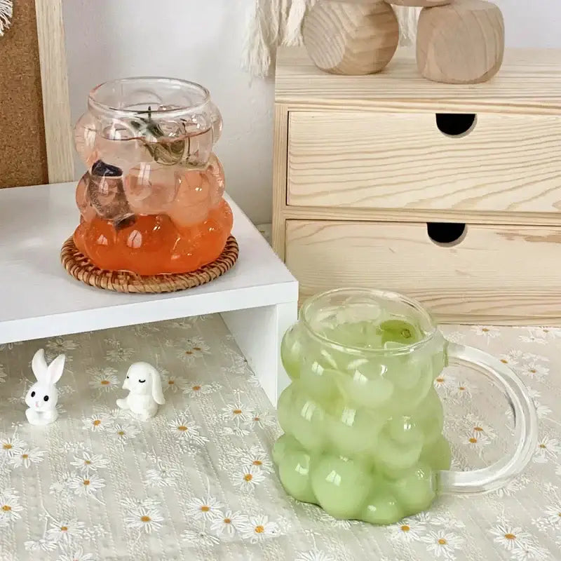 A translucent green glass mug with bubbly texture and clear handle from a glass drinking set with gold spoon