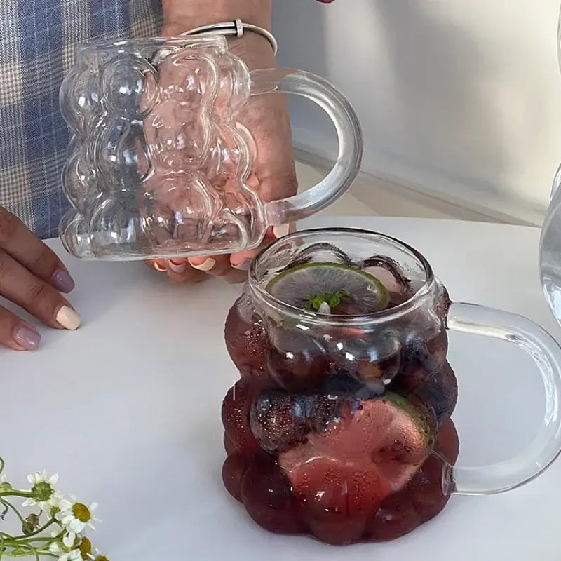 Clear glass bear-shaped pitcher filled with dark red beverage and fruit slices from textured glass drinking set