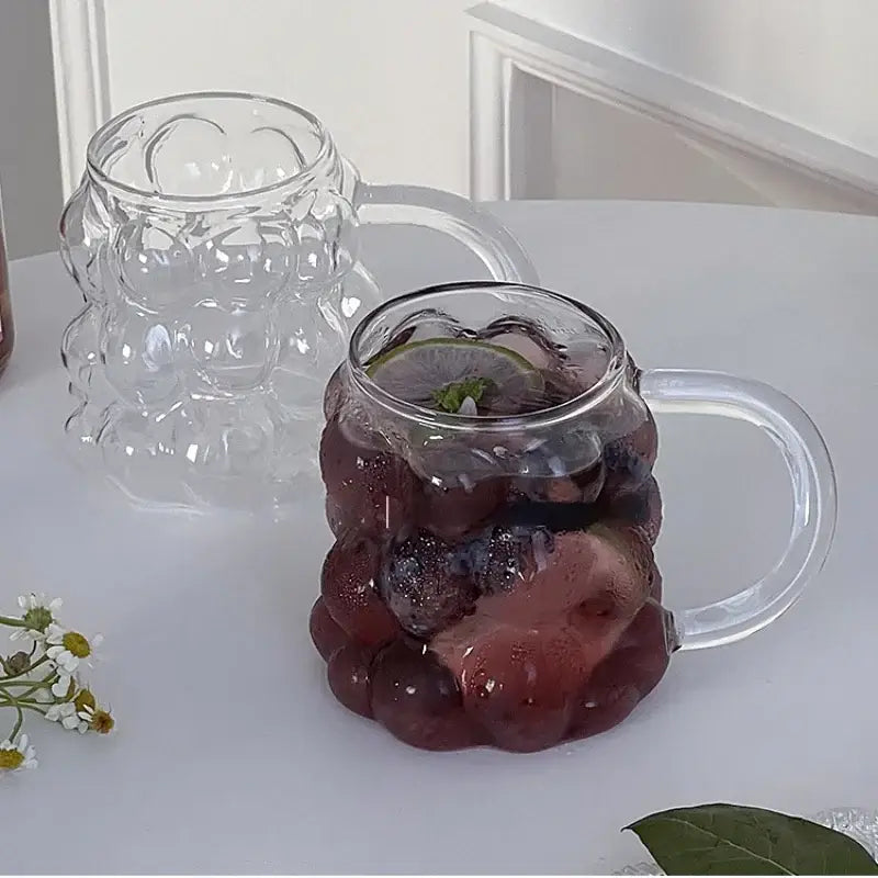 Clear glass drinking set featuring a textured grape cluster mug with transparent handle and gold spoon for dining room use