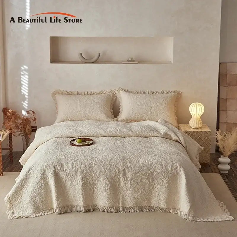 Cream cotton quilted bedspread set with textured pattern and fringed edges displayed in minimalist bedroom decorbites