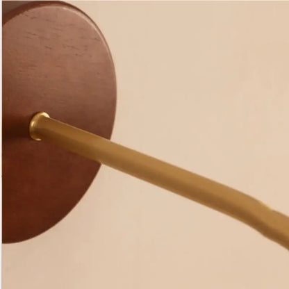 A sleek brass rod extends from a circular rich brown wooden wall plate in a textured glass and brass wall light fixture