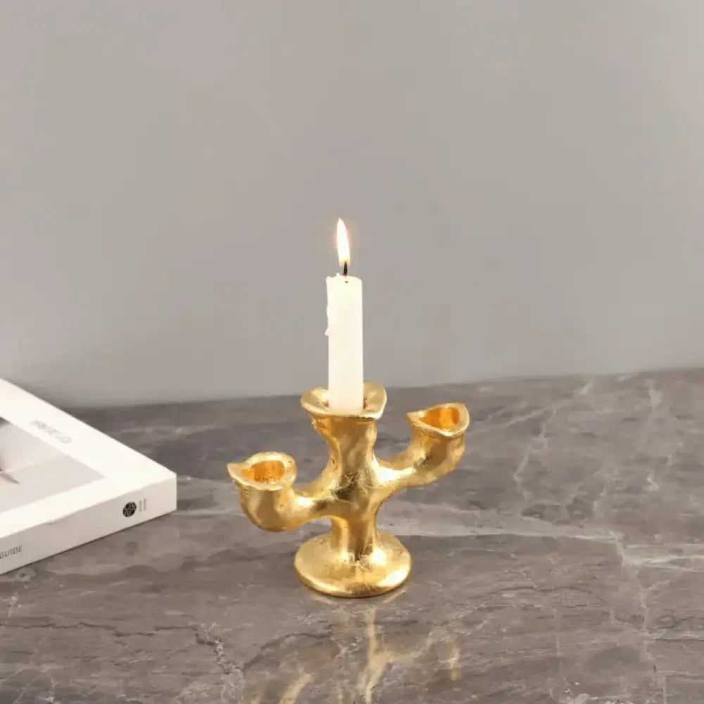 Gold resin candle holders featuring a textured organic design with three arms holding one lit white candle centerpiece
