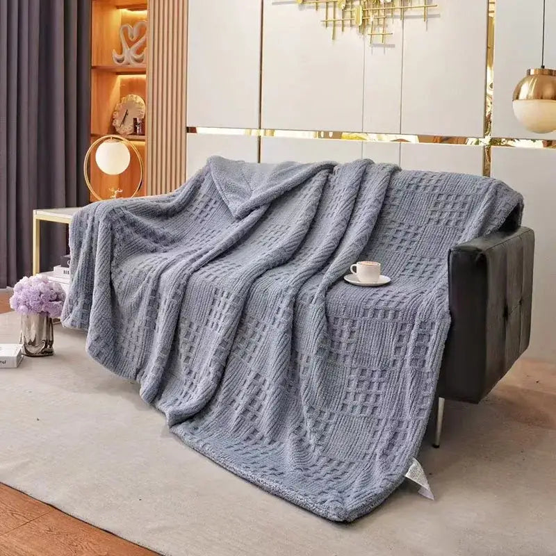 A textured gray coral fleece blanket with a diamond knit pattern draped over a modern black leather sofa