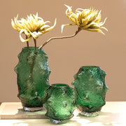 Three textured green sea cucumber glass vases with silver rims holding yellow artificial flowers for living room decor