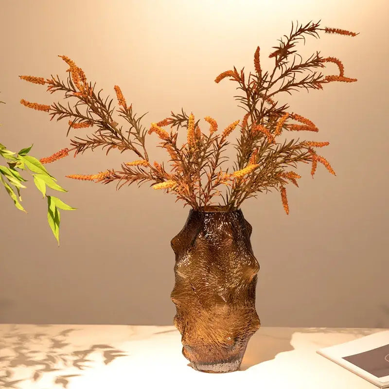 A textured amber sea cucumber glass vase with an organic form holding dried orange and brown foliage for decor