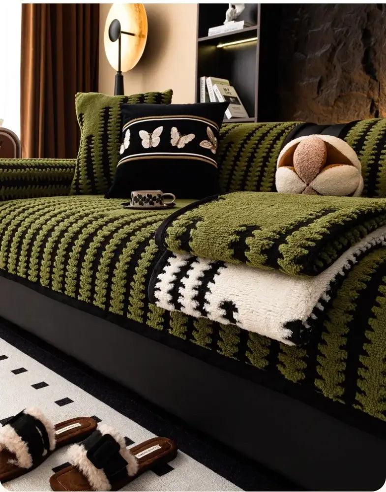 Textured olive green and black striped knitted sofa cover with white fleece blanket folded on top for living room use