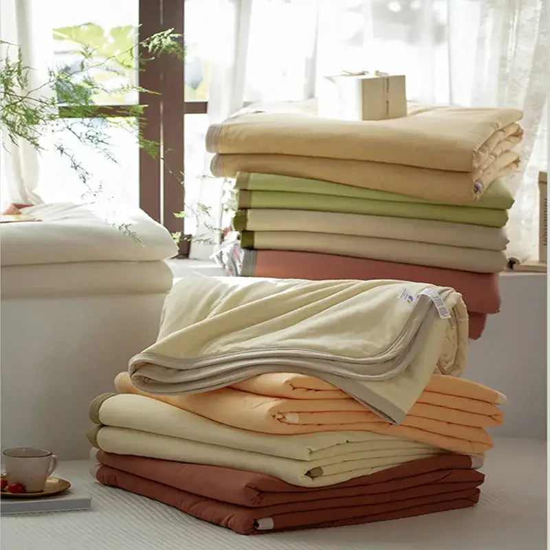 Stack of decorbites cotton summer comforters in soft pastel earthy tones with subtle textured weave for cooling bedroom use