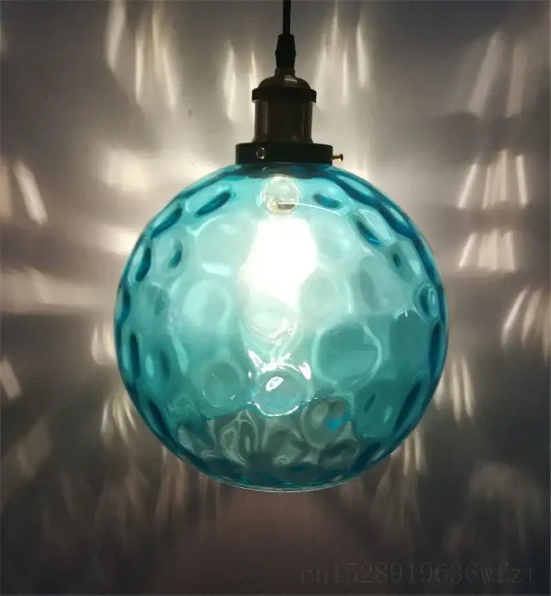 Textured turquoise blue glass ball pendant light with hammered bubble texture and dark metal fixture for kitchens