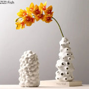 White ceramic vase set with textured bubble surface and circular cutouts featuring artificial flowers for living room decor