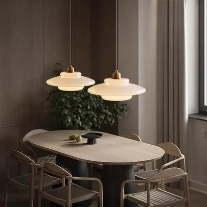 Two elegant off-white glass pendant lights with brass accents hang above a dining table in cream tiered design