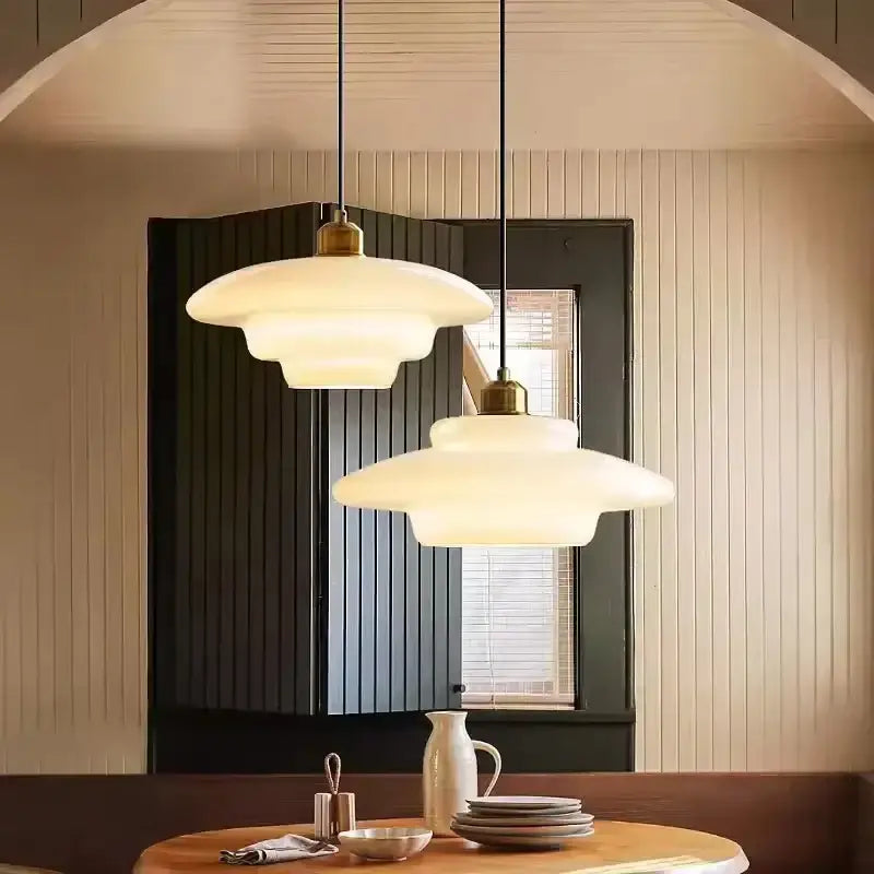 Two tiered cream glass pendant light with frosted glass and brass accents hanging from black cords for dining room