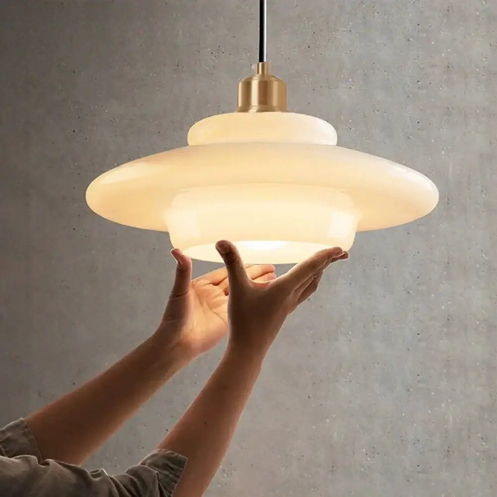 Tiered cream glass pendant light with frosted concentric tiers and brass finish metal fixture for dining room use