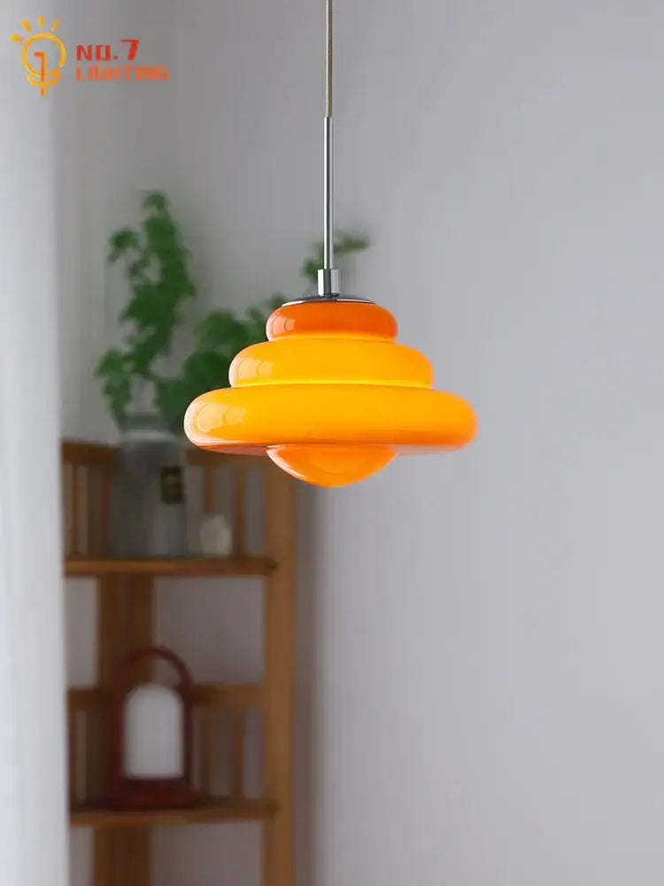 A vibrant orange tiered decorbites cream glass pendant light with a sleek chrome stem for kitchen use