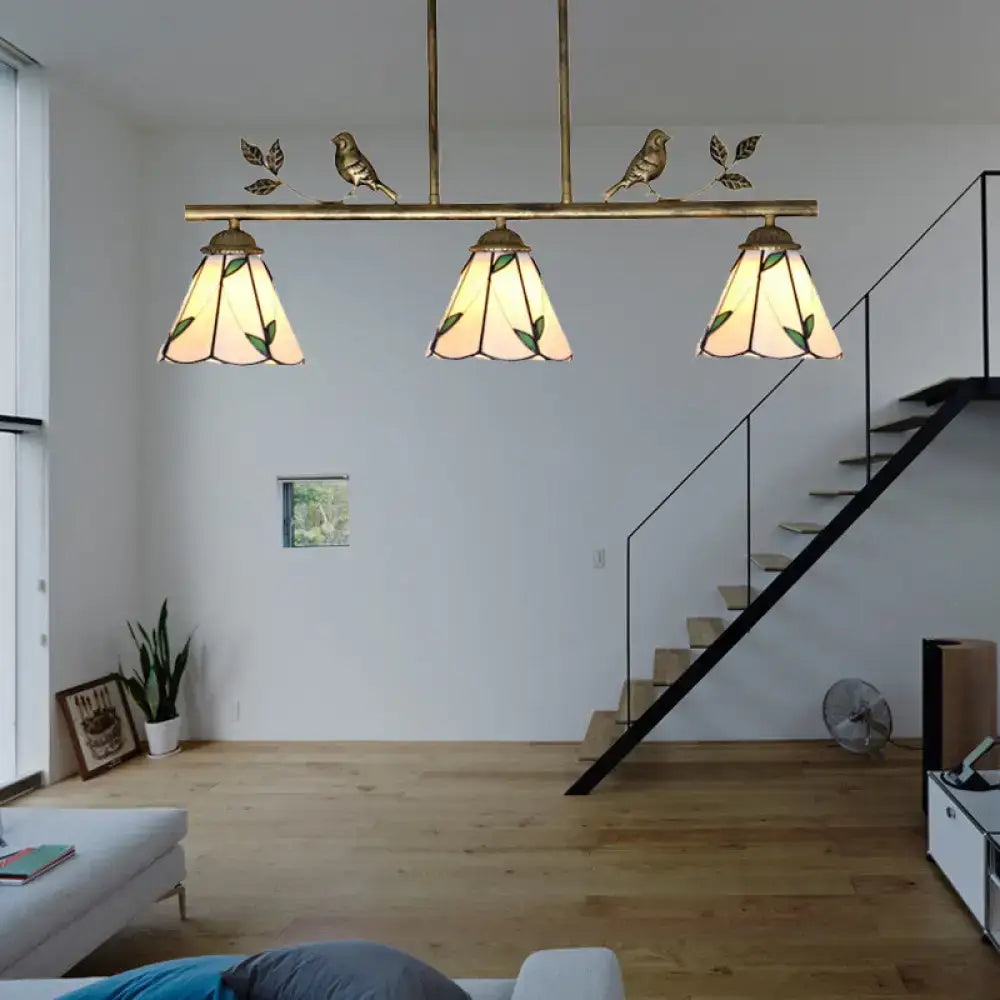 Brass-finished three-light island lighting fixture with stained glass cone shades featuring green leaf and bird motifs