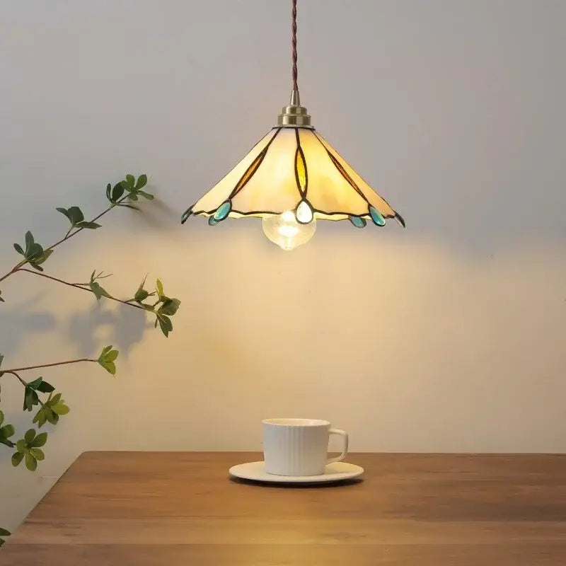 Tiffany stained glass copper led pendant lamp with warm tones brass finish and teal accents above wooden table