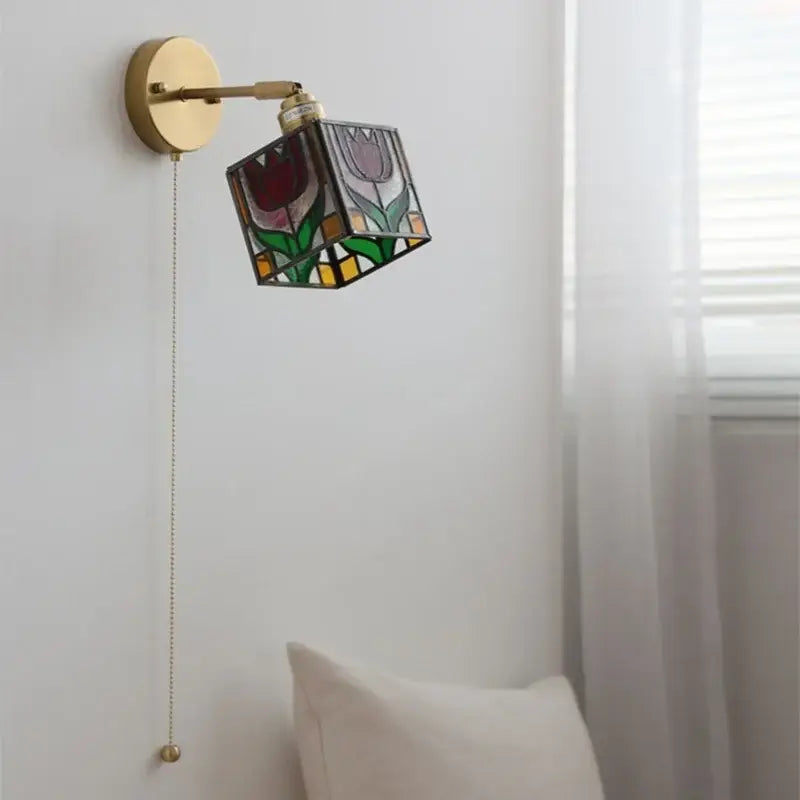 A brass-finished wall light with a colorful square glass shade featuring floral designs for decorbites colorful square lighting