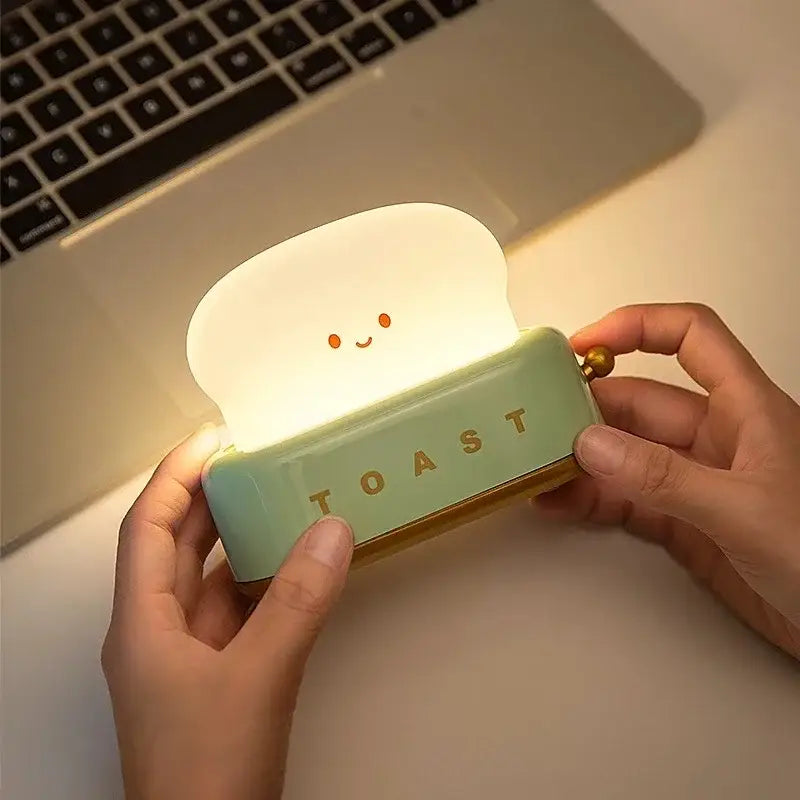A mint-green toast-shaped maker night light with a glowing white top and gold lettering for bedroom use