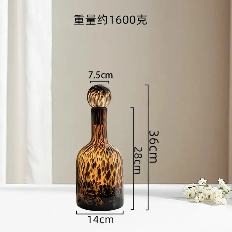 A tall slender glass decanter with tortoiseshell leopard print in dark amber and black for decorbites leopard print decor