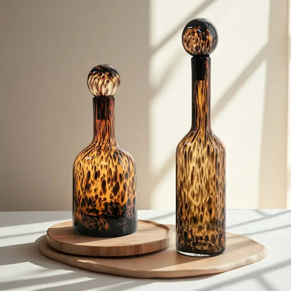 Two amber tortoiseshell glass decanters with spherical stoppers on wooden trays for decorbites leopard print decor