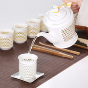 White ceramic teapot with gold accents and perforated sides pouring tea into a matching decorbites blue white porcelain cup
