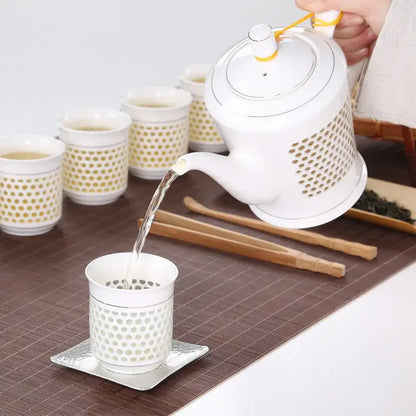 White ceramic teapot with gold accents and perforated sides pouring tea into a matching decorbites blue white porcelain cup