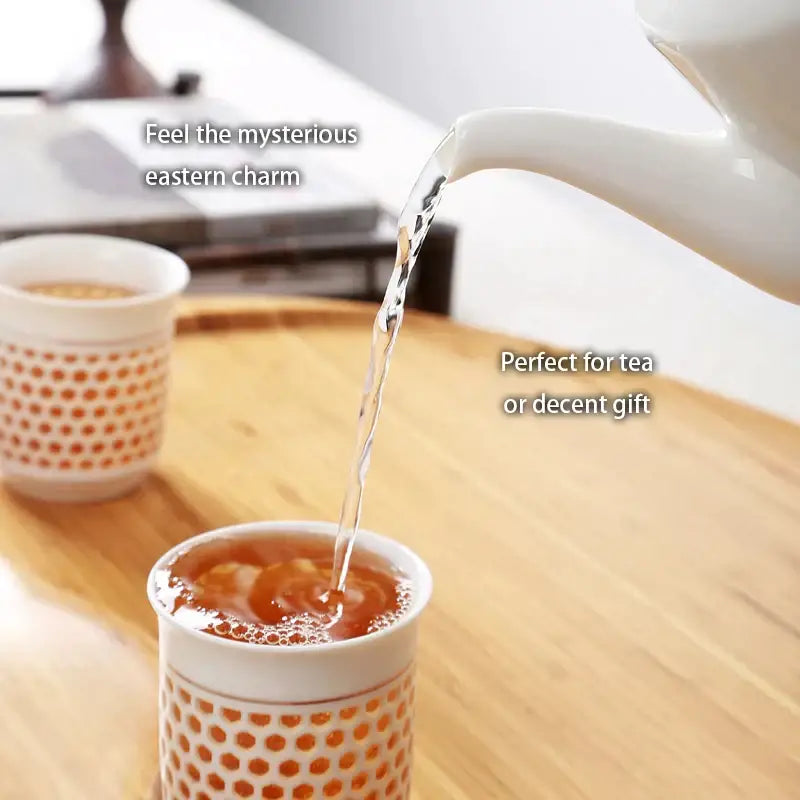 White porcelain tea set featuring a traditional blue white porcelain teapot pouring into an orange-dotted cup