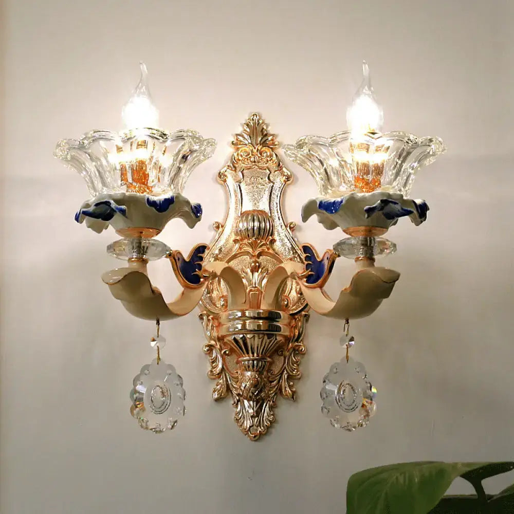 Traditional brass wall sconce light with gold-toned ornate design and crystal flower shades for living room use