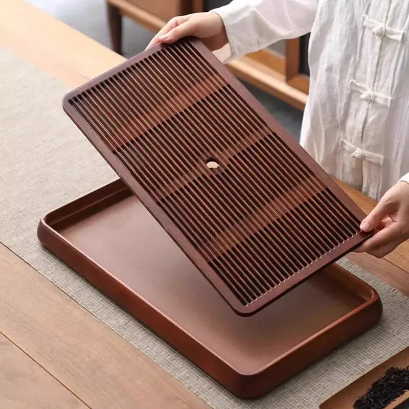 Brown bamboo tea tray with slatted top and central drainage hole for water storage in dining room use