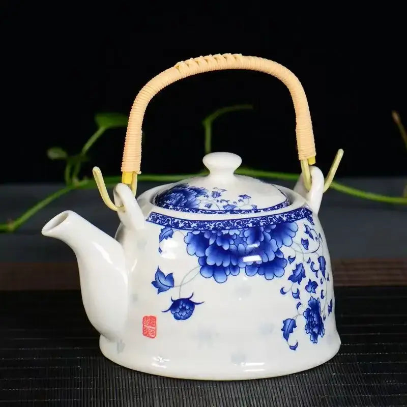 A traditional chinese white porcelain tea pot with intricate blue floral patterns and a woven bamboo handle