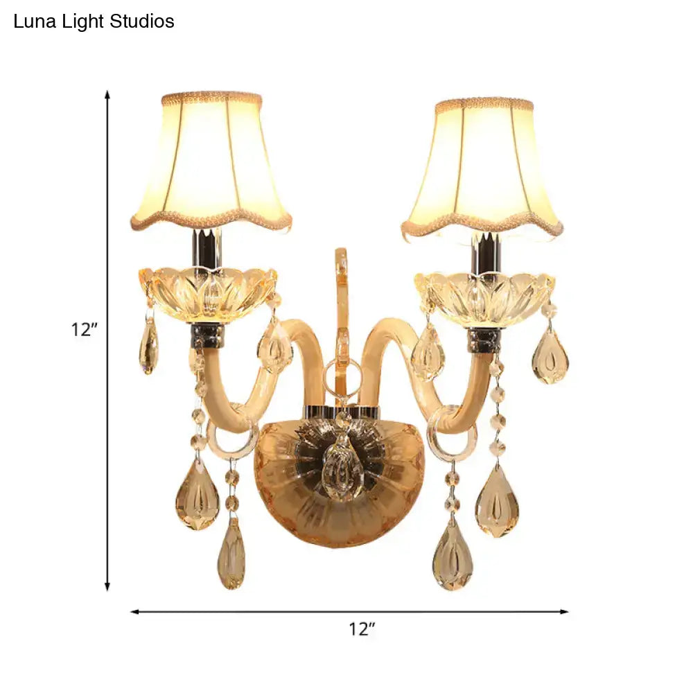 Traditional gold crystal wall sconce with two ornate arms, fabric shades, and dangling teardrop crystals for bedroom lighting