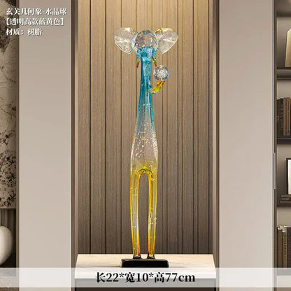 A tall translucent blue and yellow elephant floor decoration sculpture with crystal-like ears and trunk holding an ornament