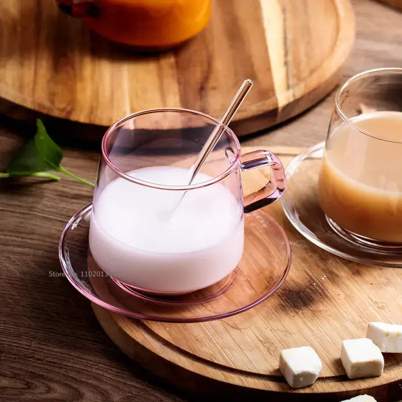 Pink-tinted glass coffee mug with matching saucer filled with creamy liquid and slender metal spoon heat resistant cup
