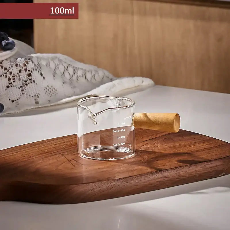 Transparent glass espresso measuring cup with wood handle and marked volume levels for precise measuring