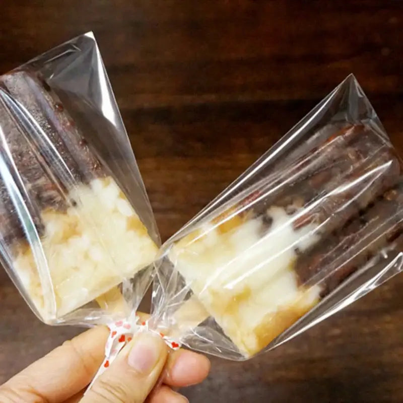 Two clear plastic-wrapped dark chocolate and creamy white ice cream popsicles in transparent pink ice cream bags with gold ribbon