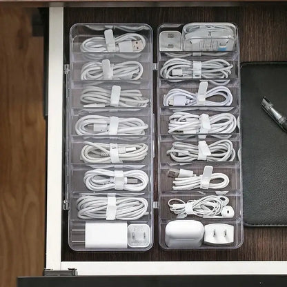 Transparent plastic cable storage box with multiple compartments holding white cables and adapters for office desk use