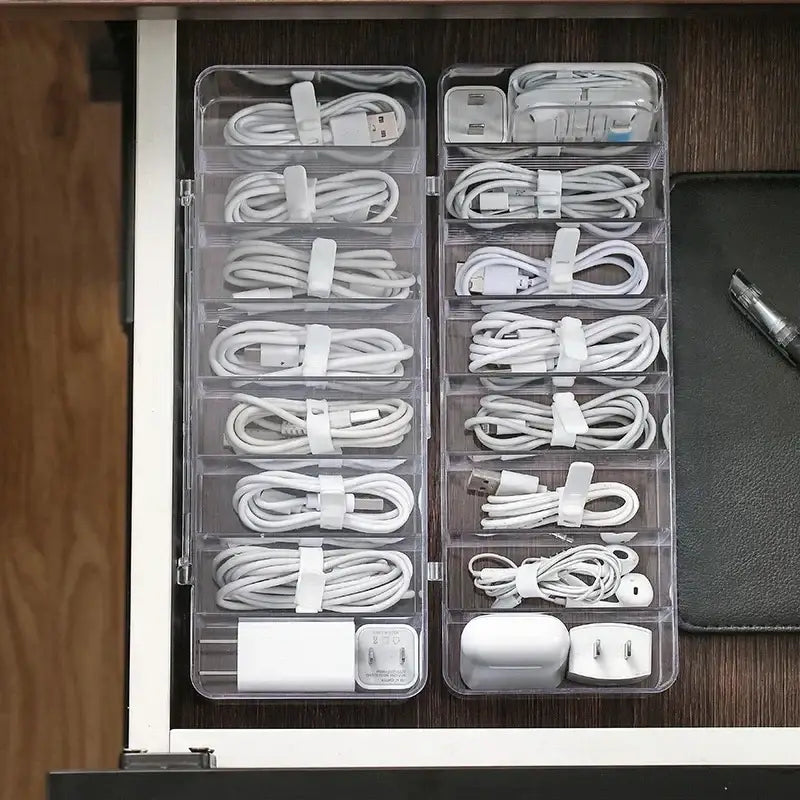 Transparent plastic cable storage box with multiple compartments holding white cables and adapters for office desk use