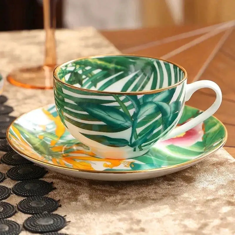 A vibrant tropical green leaf collection porcelain teacup and saucer set with yellow and pink accents rimmed in gold