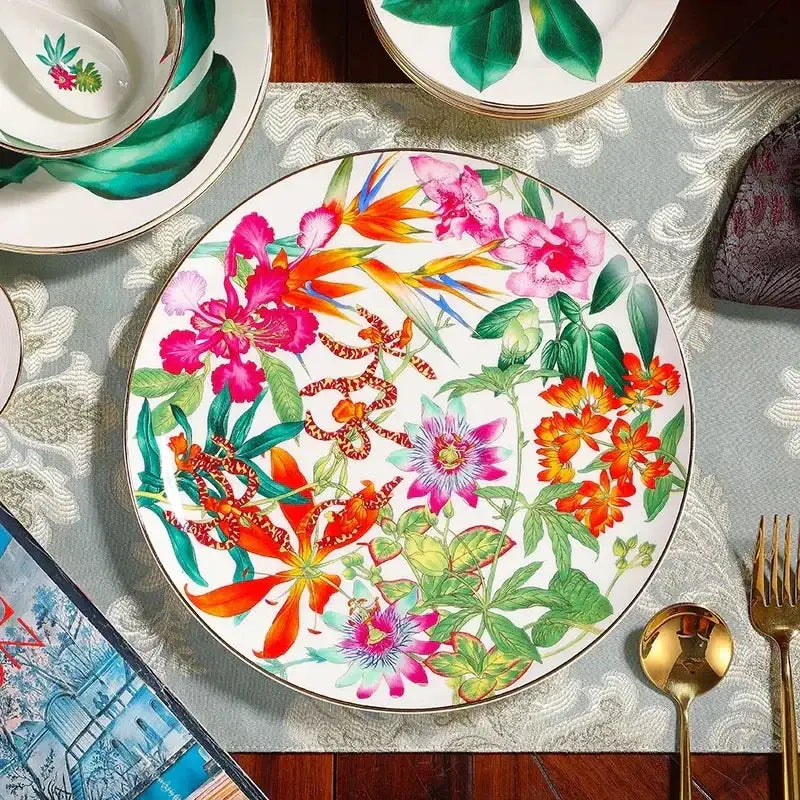 A white ceramic dinner plate from the green leaf collection featuring tropical floral design and gold-trimmed edges