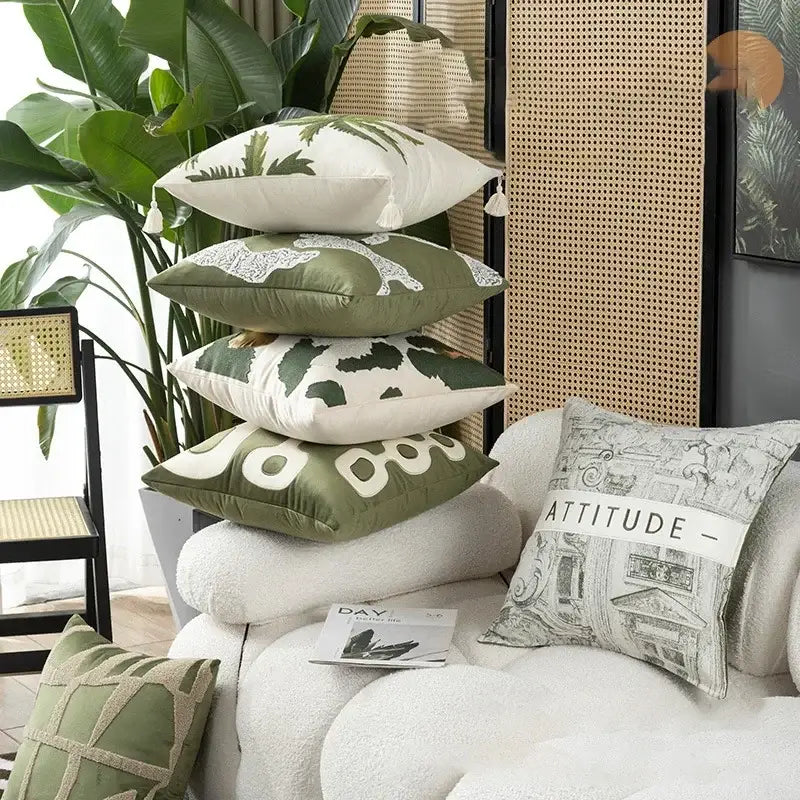 Stack of olive green and cream embroidered patchwork cushion covers with botanical and cow print designs for living room