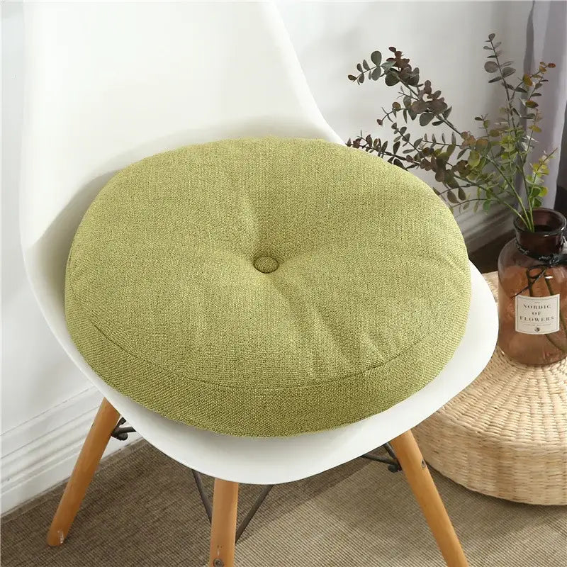 A round olive-green tufted linen seating cushion on a white chair suitable as a floor pillow seating cushion