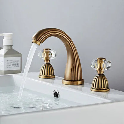 Antique brass Tuqiu gold basin faucet with crystal knob handles and curved spout flowing cold water into white sink basin